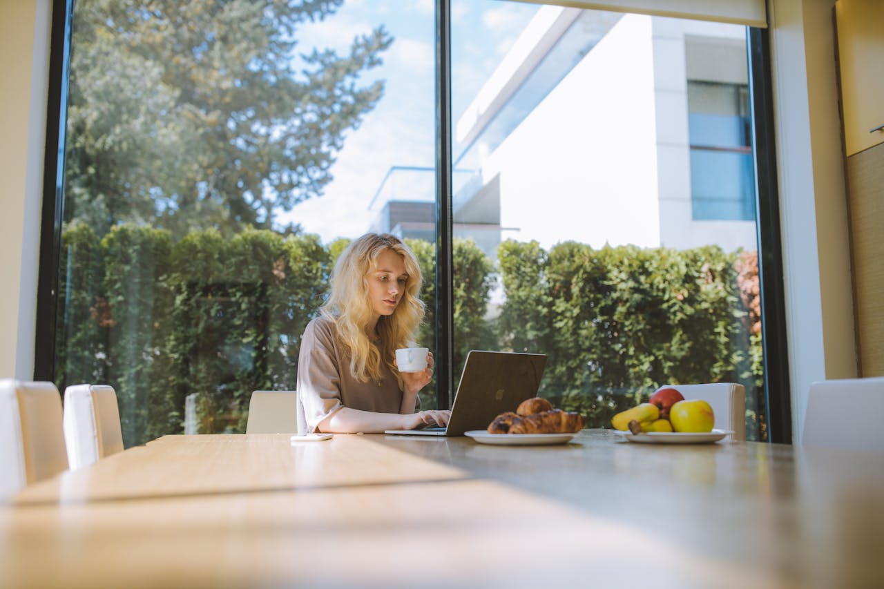 why-choose-us Blonde woman working on a laptop at home, enjoying a coffee with croissants