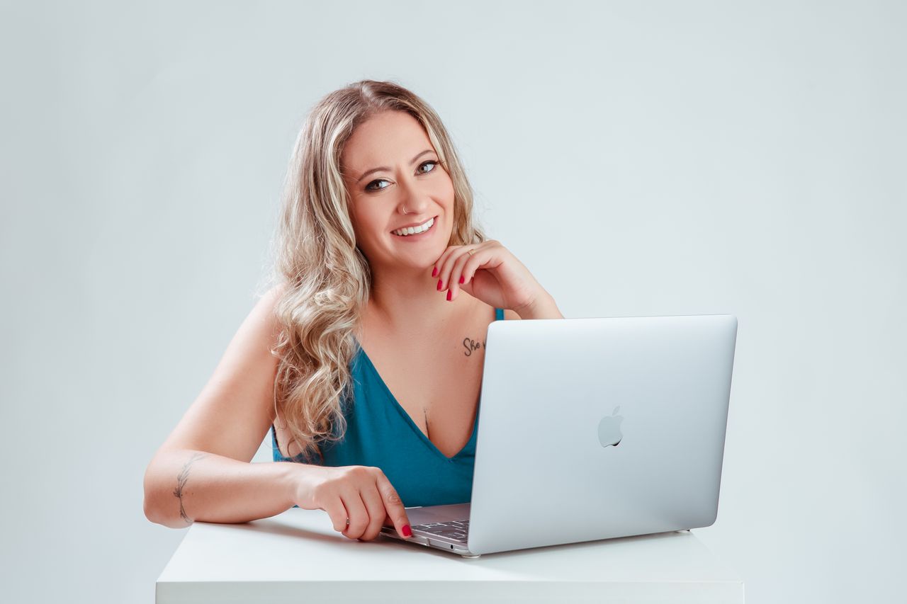 The Art of Drawing Readers In: Your attractive post title goes here A smiling woman seated at a table using a laptop, conveying positivity and engagement.